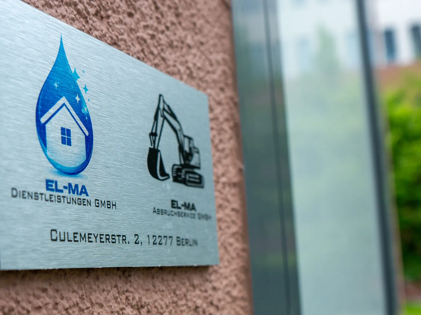 Firmenschild der ELMA Dienstleistungen GmbH neben dem Schild des Abbruchservice am Standort in Berlin