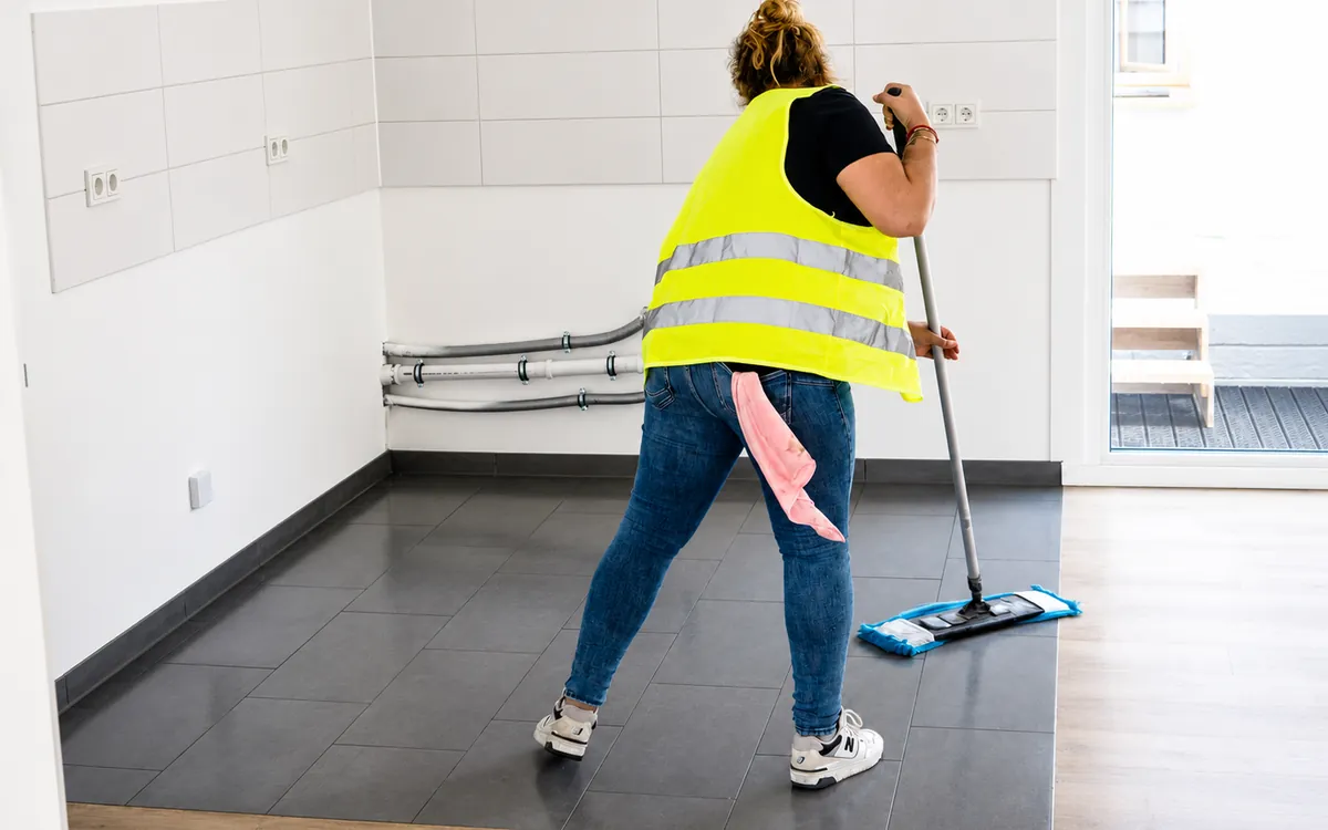Mitarbeiterin wischt den Boden einer leeren Neubauwohnung
